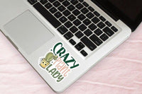A laptop with a sticker that says "Crazy Plant Lady" on the keyboard.