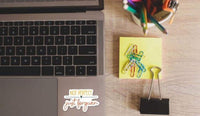 a laptop, a yellow sticky note, a binder clip, and a cup of colored pencils on a wooden surface.