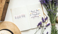 an open notebook with a motivational quote, a bouquet of purple flowers, and a straw hat on a white surface.