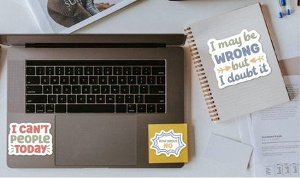 a laptop with stickers on it, along with a notebook and some papers on a desk.
