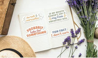 a notebook with various stickers on it, along with a hat, a bunch of lavender flowers, and some other items.