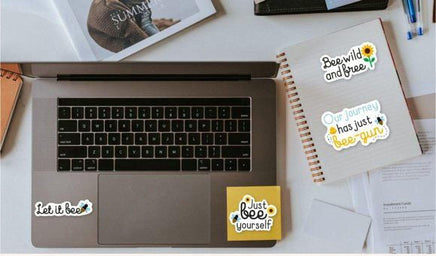 a laptop with stickers on it, along with some papers and other items on a desk.