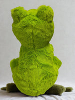 A large, plush green frog toy is sitting on a white surface.