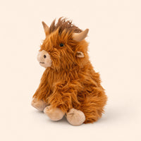 A plush toy of a Highland cow, with its distinctive shaggy fur and large horns, is sitting on a plain background.