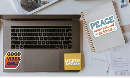 a laptop with stickers on it, along with a notebook and some papers on a desk.