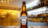 A brown beer bottle with a sticker that says "GOOD FRIENDS & GREAT BEER" is placed on a wooden surface.