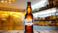 A brown beer bottle with a label that says "Drink happy thoughts" is placed on a wooden surface against a blurred background of a bar or restaurant.