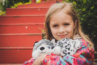 A young girl with blonde hair is holding a stuffed animal, smiling at the camera.