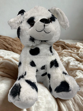 A stuffed dalmation dog toy is sitting on a bed with a beige blanket.