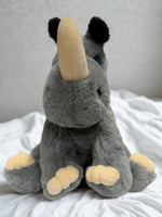 A plush toy rhinoceros with a tan horn sits on a white bedspread.