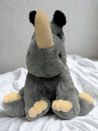A plush toy rhinoceros with a tan horn sits on a white bedspread.