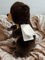 A brown plush bear toy is sitting on a beige blanket.