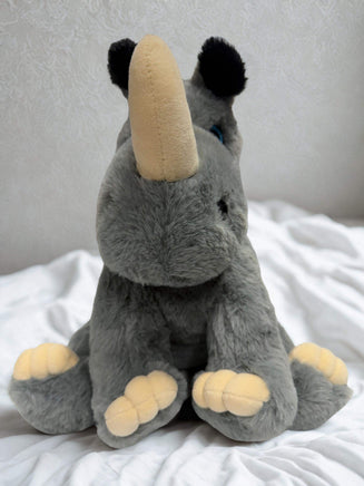 A plush toy rhinoceros with a tan horn sits on a white bedspread.