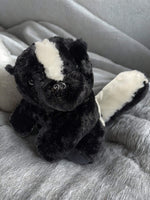 A black and white stuffed animal toy, resembling a skunk or a similar animal, is sitting on a gray blanket.