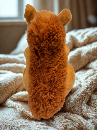 A plush toy of a squirrel sitting on a bed with a white blanket.