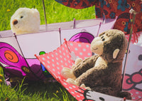 Two stuffed animals, a monkey and a teddy bear, are sitting together under a colorful umbrella in a grassy field.