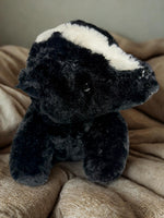 A black and white stuffed animal toy is sitting on a beige blanket.