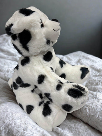 A white and black spotted teddy bear is sitting on a white bedspread.
