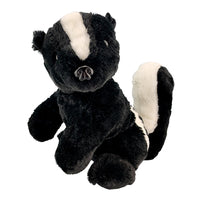 A plush toy of a black and white skunk is sitting on a white background.