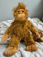 A plush toy of an orangutan sitting on a bed with a white blanket.