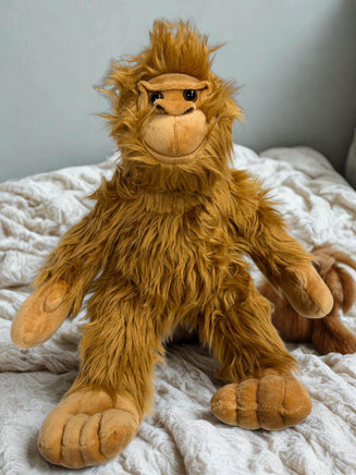 A plush toy of an orangutan sitting on a bed with a white blanket.