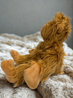 A plush toy bear with shaggy fur is sitting on a white blanket.