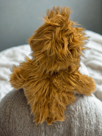 A fluffy, brown teddy bear sits on a gray blanket, its soft fur and cozy appearance creating a warm and inviting scene.