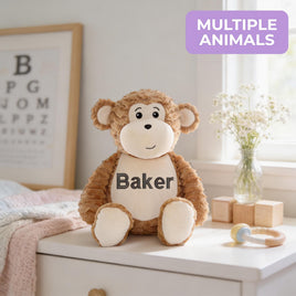 A brown stuffed monkey toy with the name "Baker" printed on it, sitting on a white dresser next to a vase of flowers and a baby rattle.