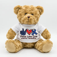 A brown teddy bear wearing a white t-shirt with a peace sign and a blue ribbon symbolizing diabetes awareness.
