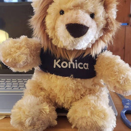 Tan lion plush wearing a navy custom t-shirt with the name Konica printed in white