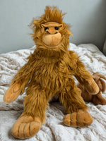 A plush toy of an orangutan sitting on a bed with a white blanket.