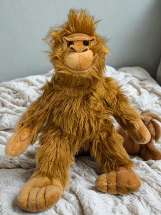 A plush toy of an orangutan sitting on a bed with a white blanket.