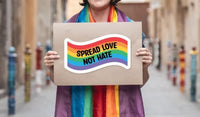 A person wearing a rainbow scarf is holding a sign that says "SPREAD LOVE NOT HATE".