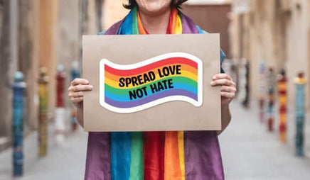 A person wearing a rainbow scarf is holding a sign that says "SPREAD LOVE NOT HATE".