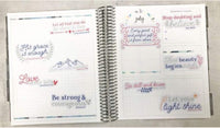 The image is an open spiral-bound notebook with various inspirational quotes and Bible verse references. The notebook is open to a page titled "July" and contains a list of Bible verse references, such as "His grace is enough" and "Be strong and courageous." The notebook also features a page titled "Monthly Goals" with a list of goals and a Bible verse reference. The overall layout and content suggest that the notebook is being used as a tool for personal