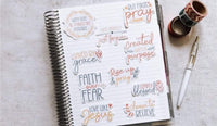 a spiral-bound notebook with various inspirational quotes and phrases written on its pages, along with a pen and some tape.