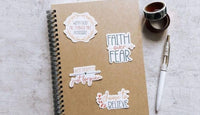 a brown spiral notebook with various stickers and a pen on a white surface.