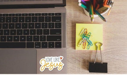 a laptop, a yellow sticky note, a binder clip, and a cup of colored pencils on a wooden surface.