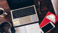 a laptop, a notebook, a smartphone, and some stationery items such as a pen and a coffee cup, all arranged on a wooden surface.