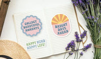 a notebook with two stickers on it, along with a bouquet of purple flowers and a straw hat.