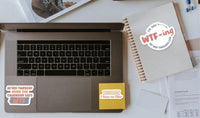 a laptop with stickers on it, along with some papers and other office supplies on a desk.