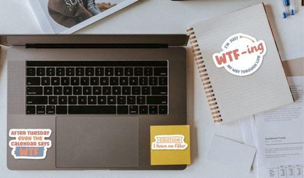 a laptop with stickers on it, along with some papers and other office supplies on a desk.