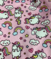 a close-up view of a pink fabric with a repeating pattern of white unicorn illustrations, along with various other whimsical elements such as clouds, rainbows, and stars.