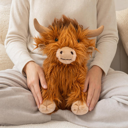 A person is sitting on a bed, holding a large stuffed animal resembling a furry, horned creature with a big smile on its face.