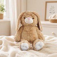 A brown stuffed bunny rabbit toy sits on a white blanket in a cozy bedroom setting.