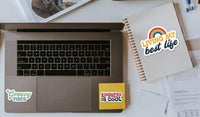 a laptop with stickers on it, along with a notebook and some papers on a desk.