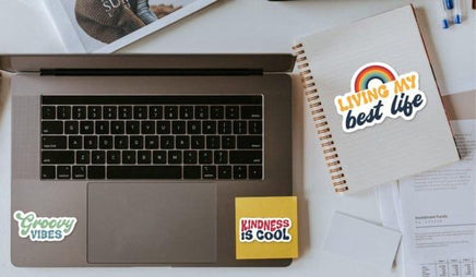 a laptop with stickers on it, along with a notebook and some papers on a desk.