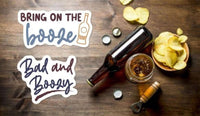 a wooden table with various items, including a bottle of beer, a glass, a bowl of chips, and a bottle opener. There is also a sticker with the text "Bad and Bozy" and a bottle cap.