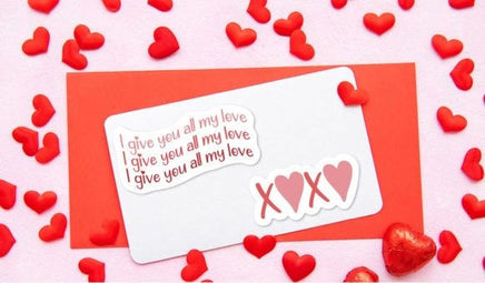 a Valentine's Day-themed arrangement with a white card, a red envelope, and red heart-shaped candies scattered around.