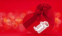 A heart-shaped gift box with a bow and the text "Love is sweet" on it, set against a red background with bokeh lighting effects.